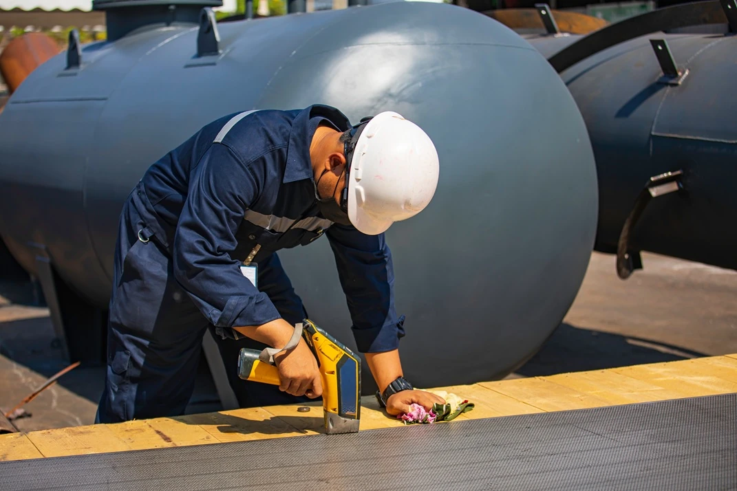 Technician wearing safety gear performing positive material identification testing on industrial equipment with handheld XRF analyser